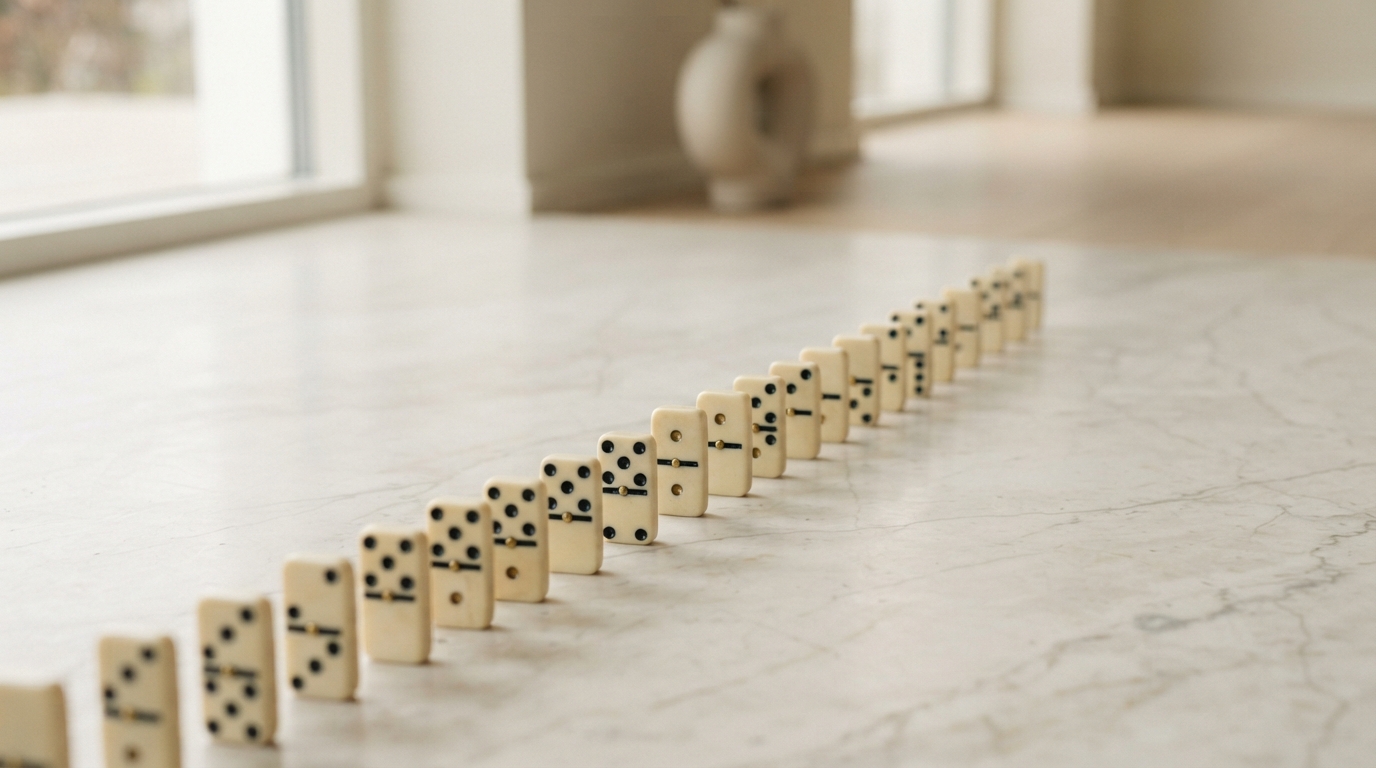 A long row of dominoes standing on a pale marble counter in a bright room